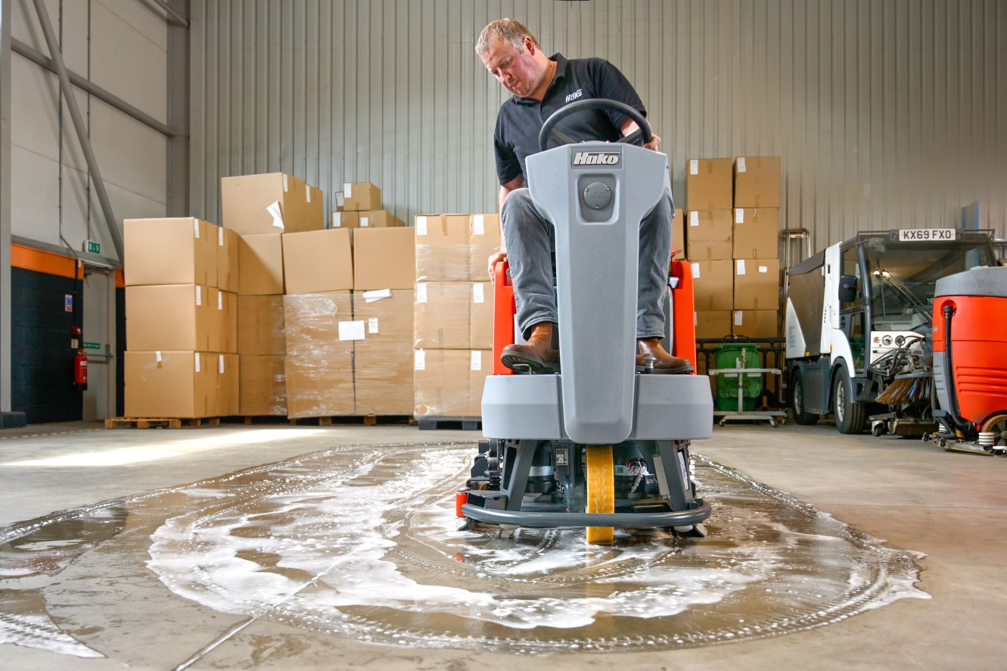 A Hako ride-on scrubber dryer cleaning a floor in a warehouse.